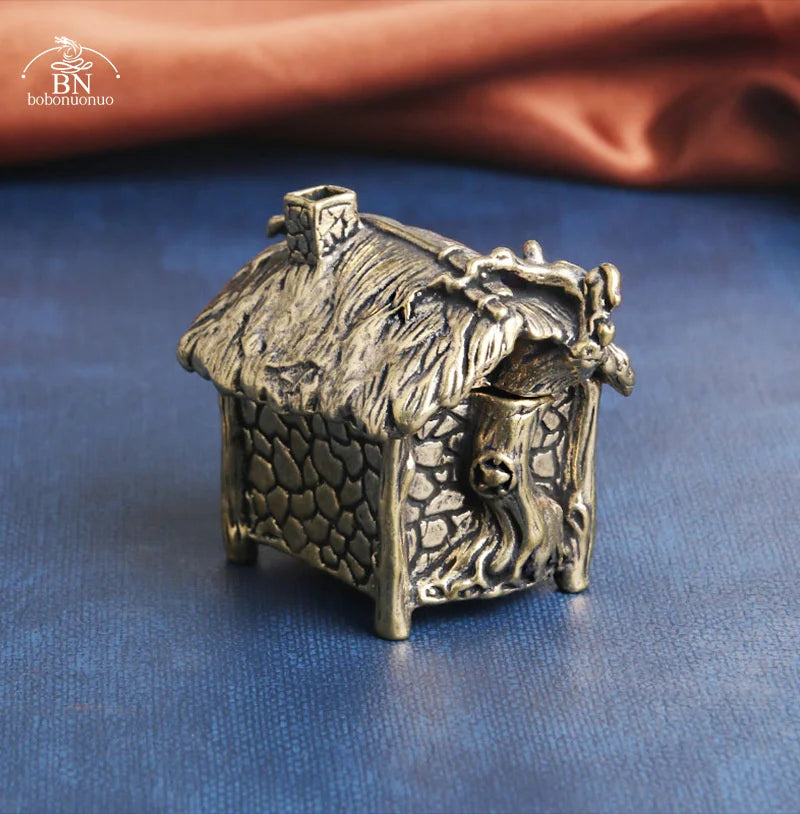 Bronze miniature house with thatched roof on a blue surface, brand 'BN' visible