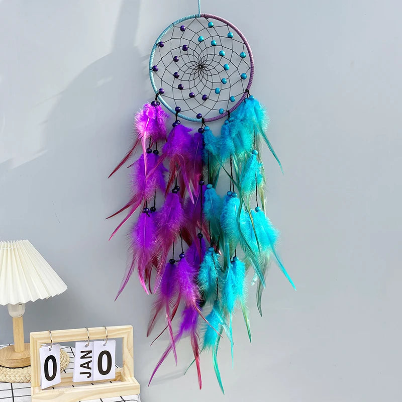 Colorful dreamcatcher with feathers on a light gray wall.