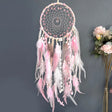 Pink and white dreamcatcher with feathers against a gray background