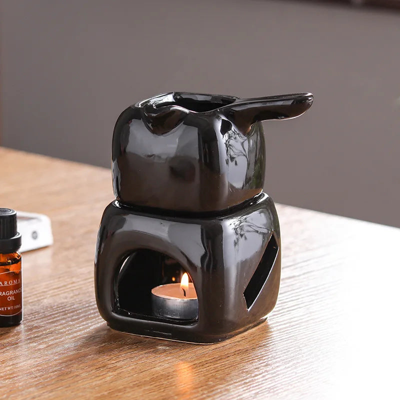 Black ceramic oil burner with a lit candle on a wooden surface