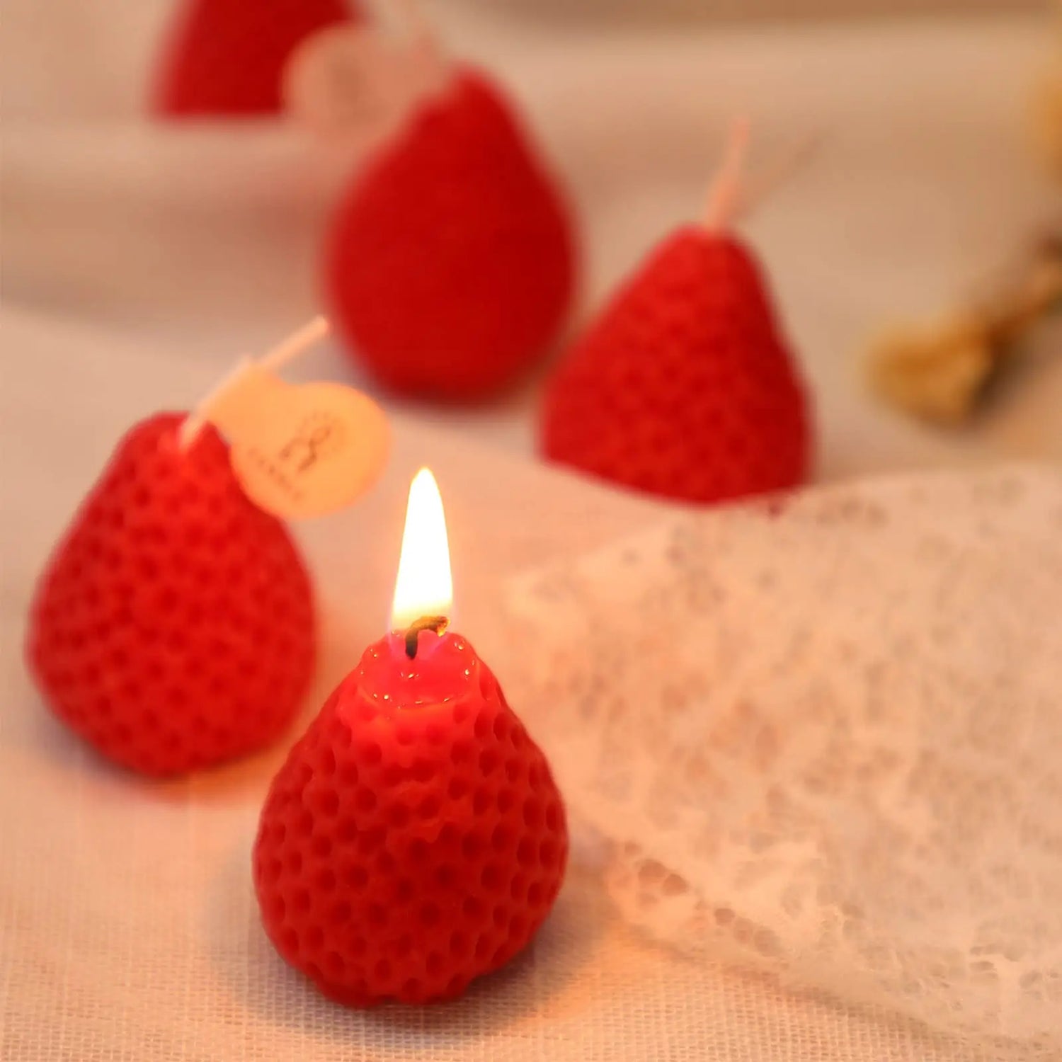 Red textured candles with a lit one on a beige fabric background