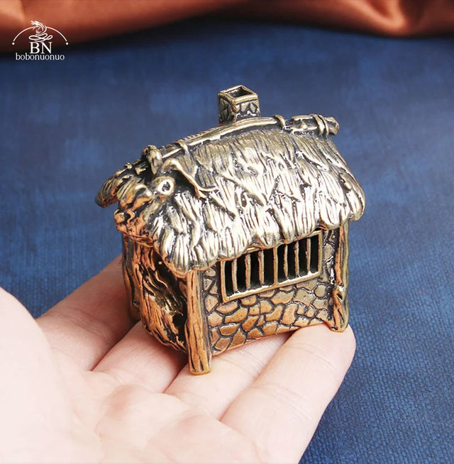 Bronze miniature hut held in a hand against a blue background