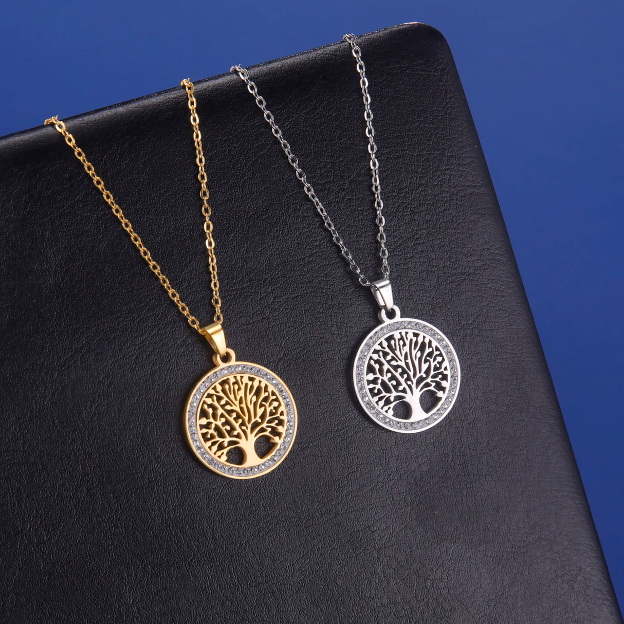 Two tree-shaped pendants on gold and silver chains against a black background
