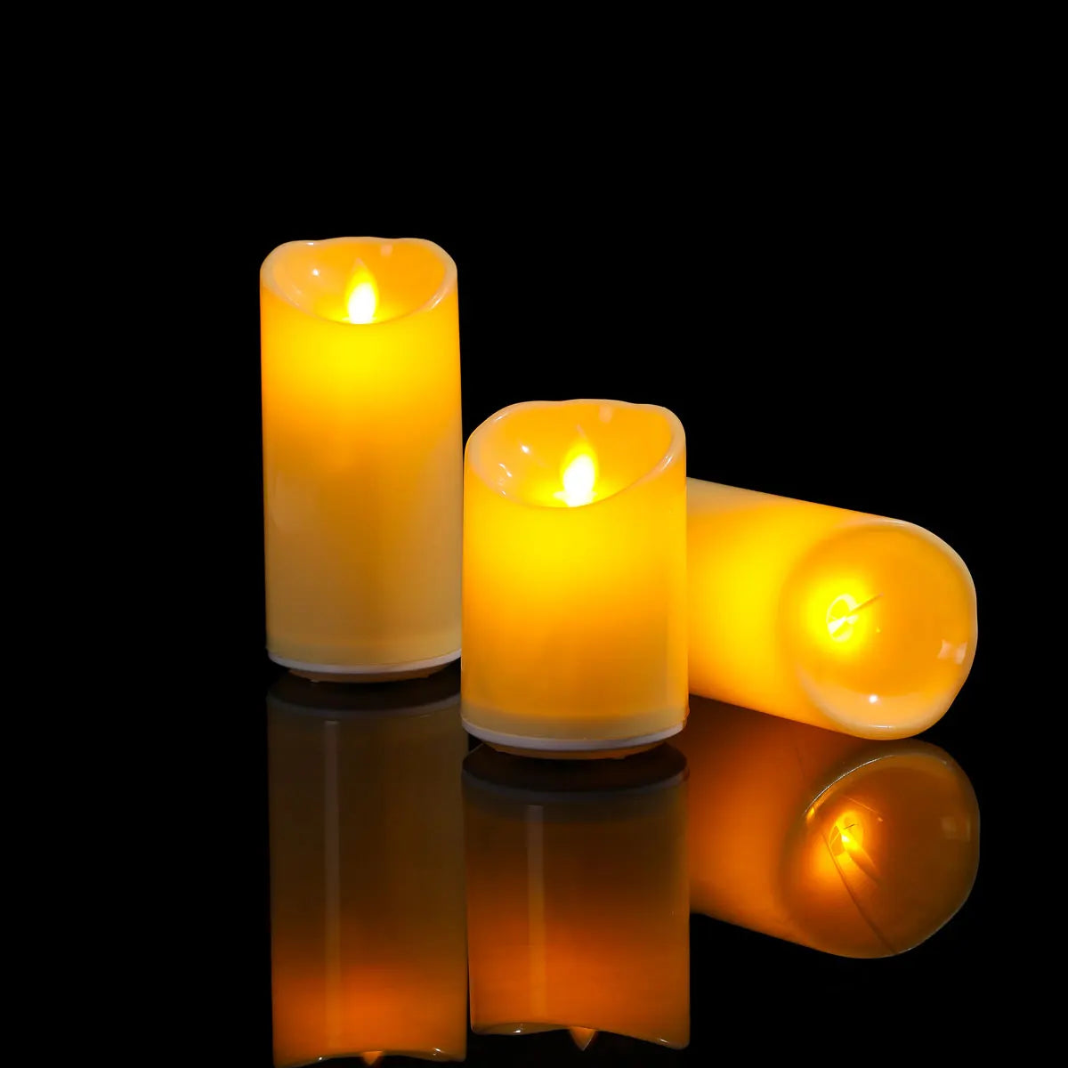 Three lit candles of different sizes on a reflective surface with a black background