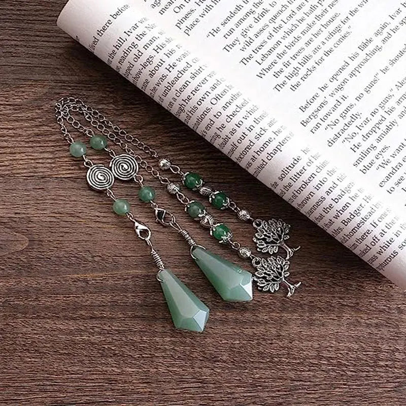 Necklace with green beads and silver accents on a wooden surface with a book underneath
