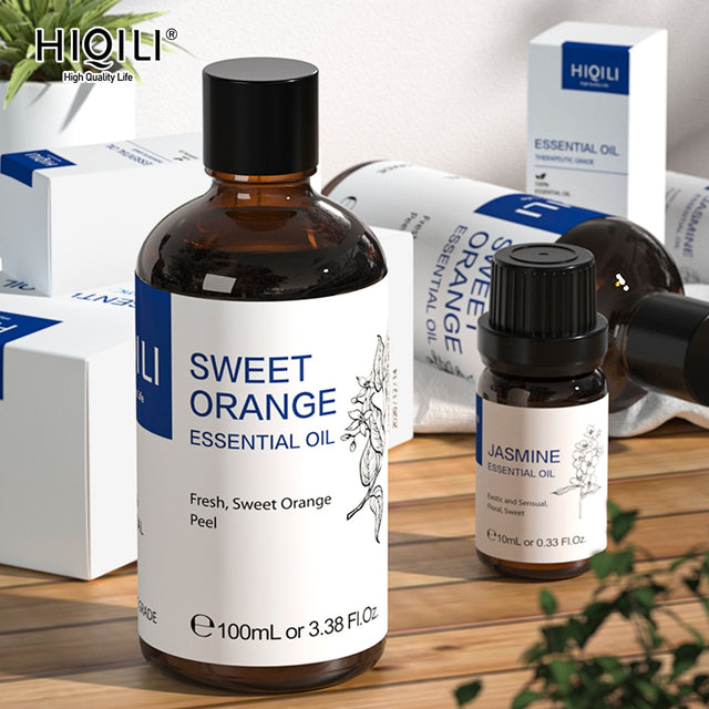 Two bottles of essential oil, one labeled 'Sweet Orange' and the other 'Jasmine', on a wooden surface with boxes in the background.