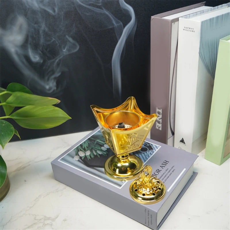 Gold incense burner with smoke on a book with plant and books in the background