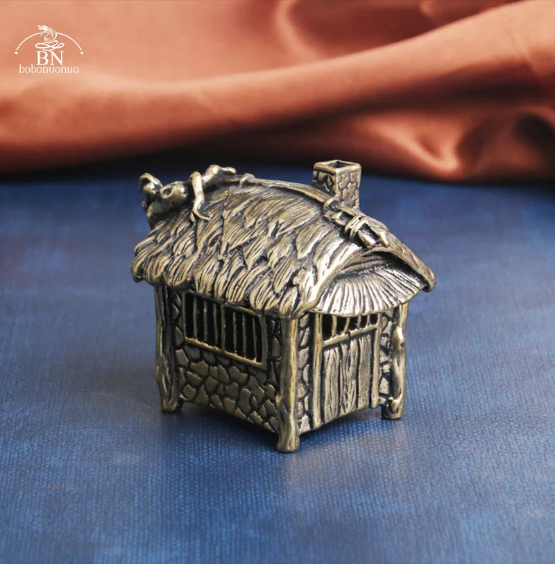 Bronze miniature house with thatched roof on a blue surface