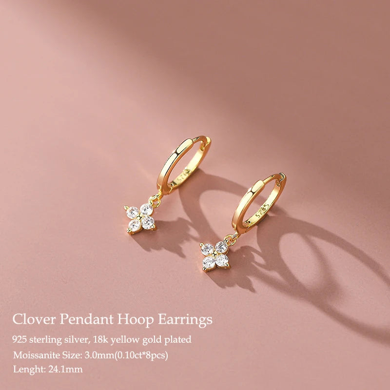 Gold clover pendant hoop earrings on a pink background
