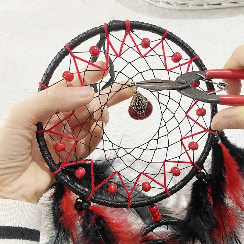Hand holding a small dreamcatcher with red and black strings, feathers, and a pendant.