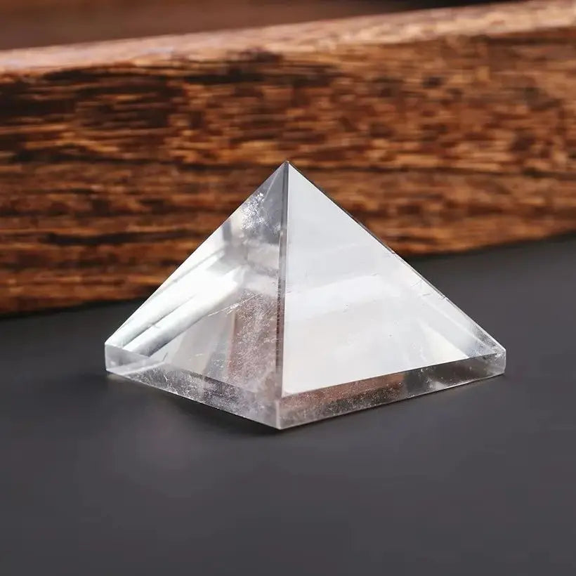 Clear crystal pyramid on a dark surface with a wooden background
