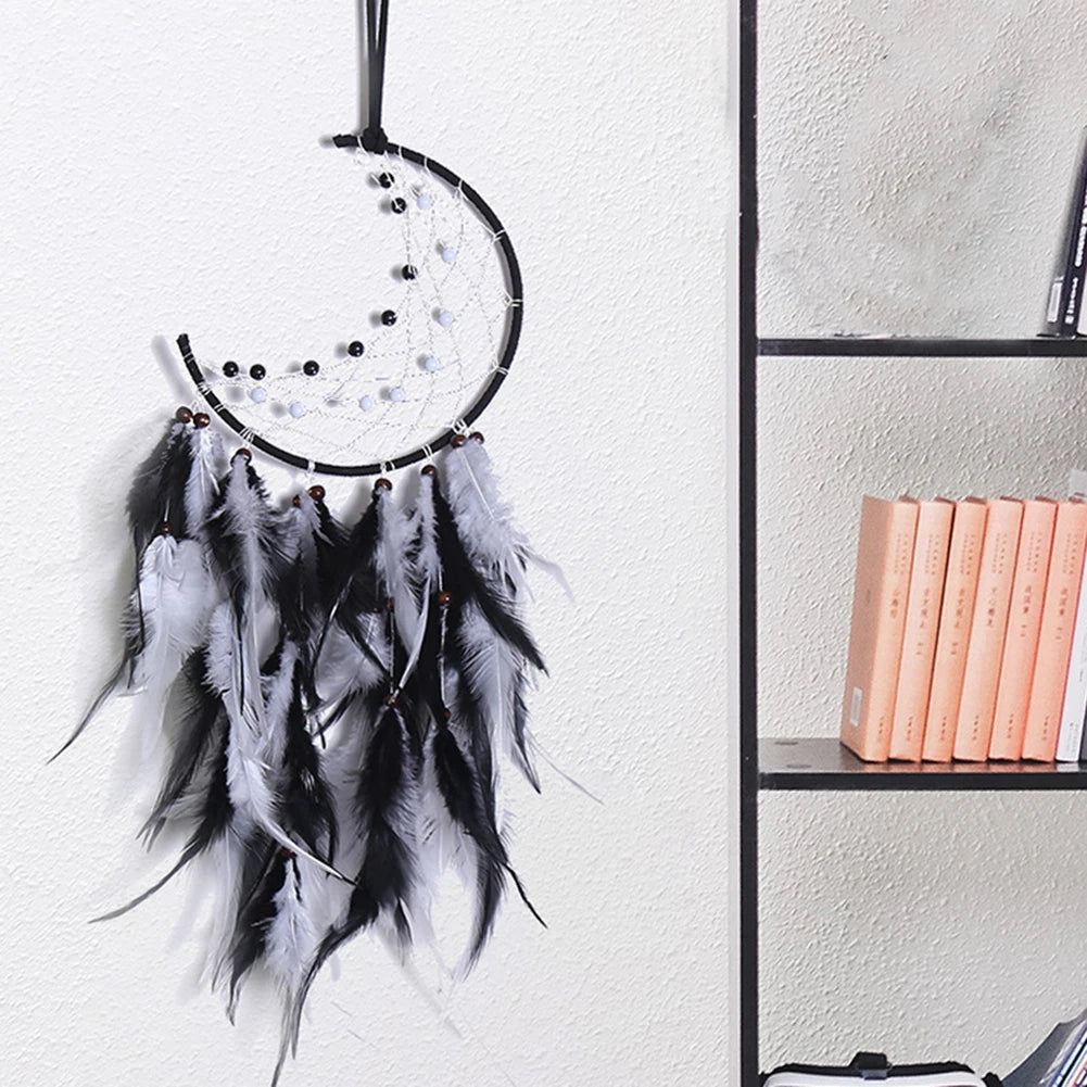 Black and white dreamcatcher hanging on a white wall with books on a shelf in the background.