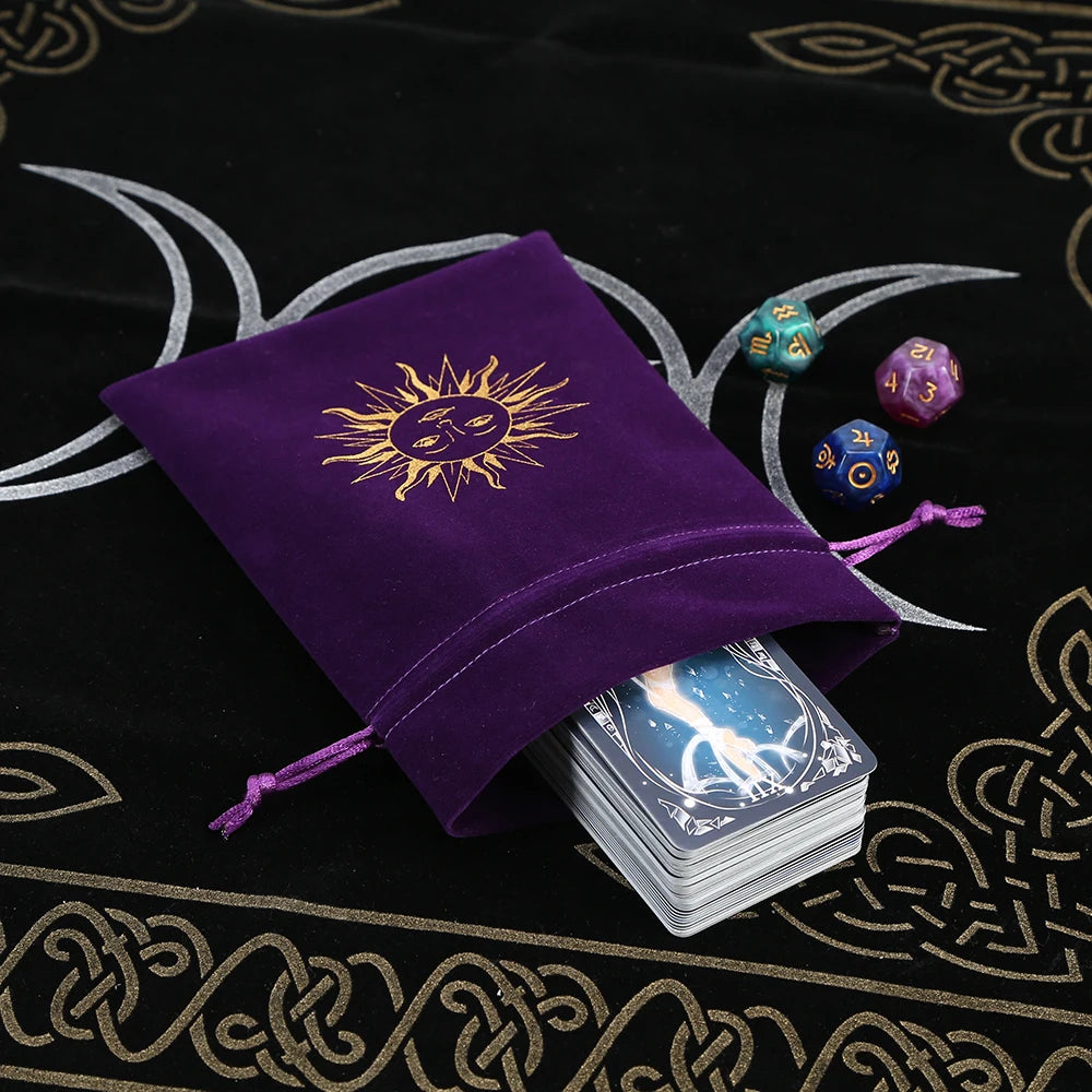 Purple drawstring bag with sun design on a black cloth with star and moon patterns, featuring playing cards and dice.