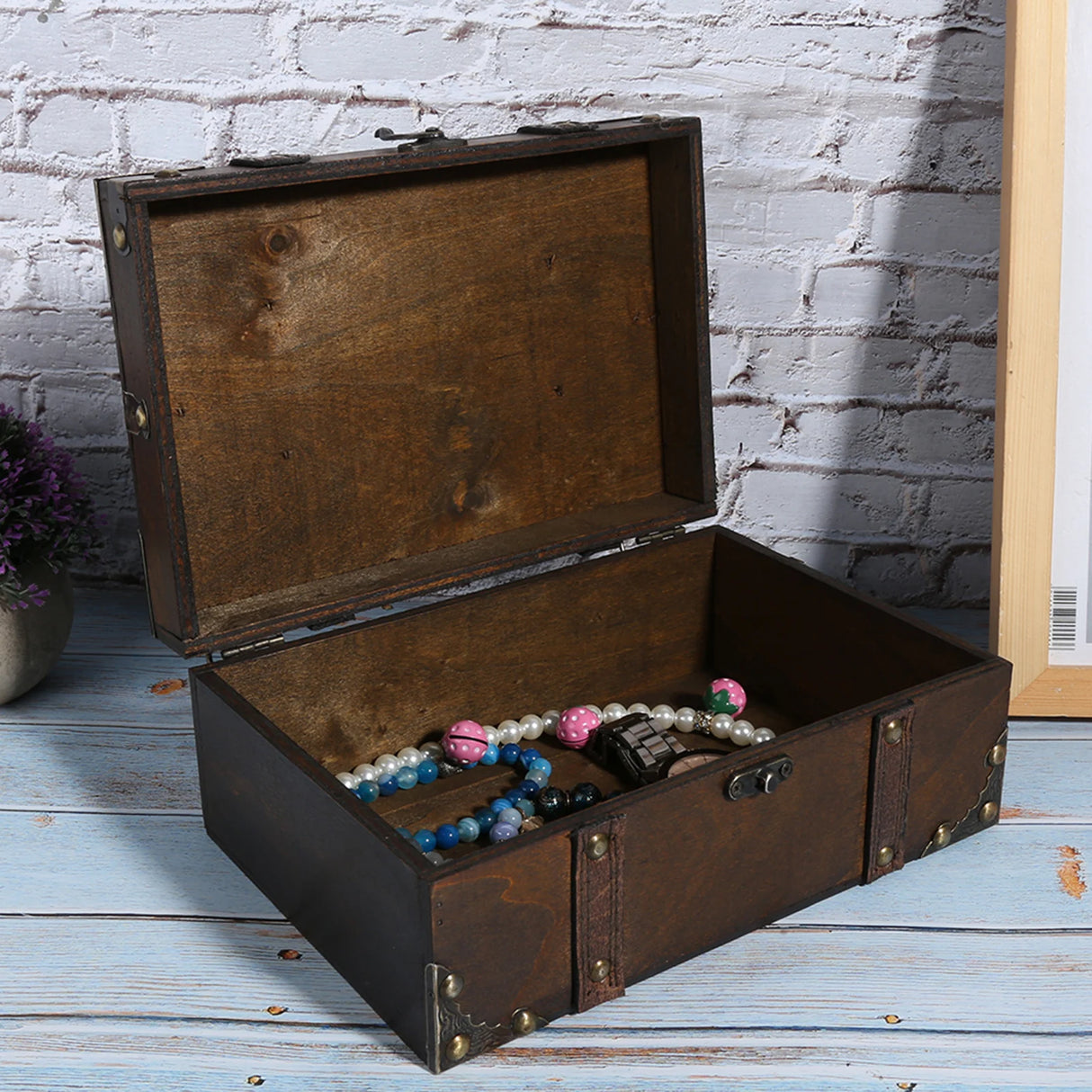 Open wooden treasure chest with jewelry on a wooden floor against a white brick wall.