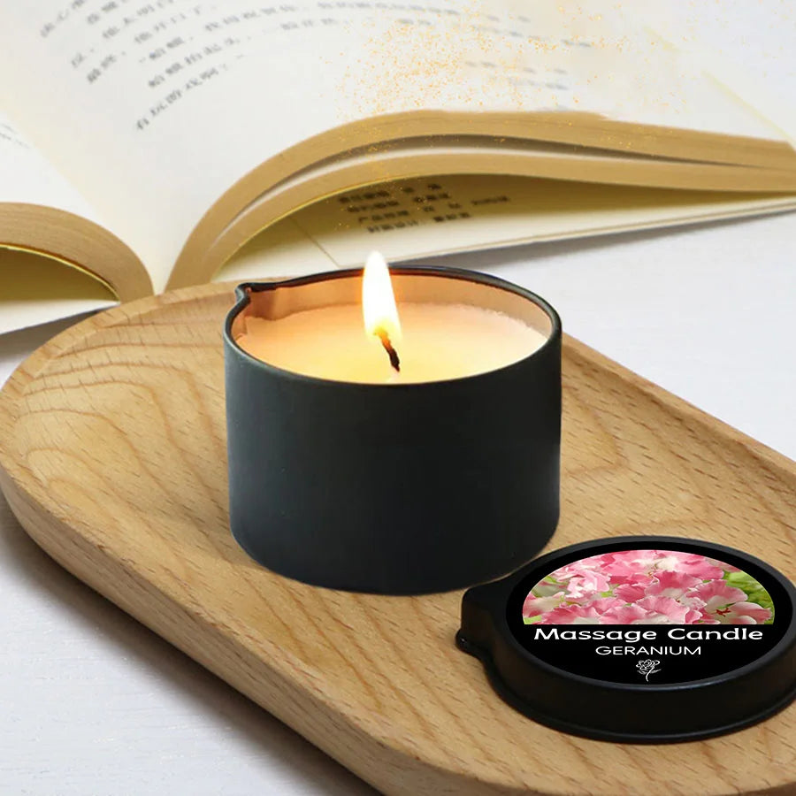 Black candle with a lit wick on a wooden tray next to an open book