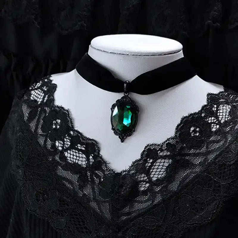 Black lace garment with a black choker necklace featuring a green gemstone on a mannequin against a dark background.