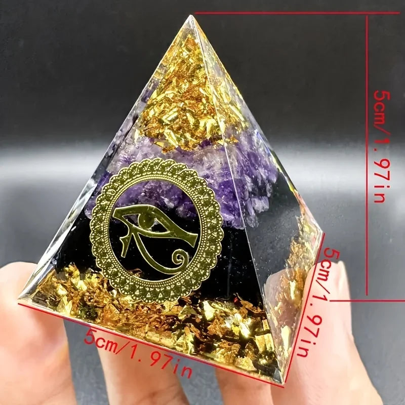 Pyramid-shaped crystal with gold leaf and amethyst, held by a hand, against a dark background.