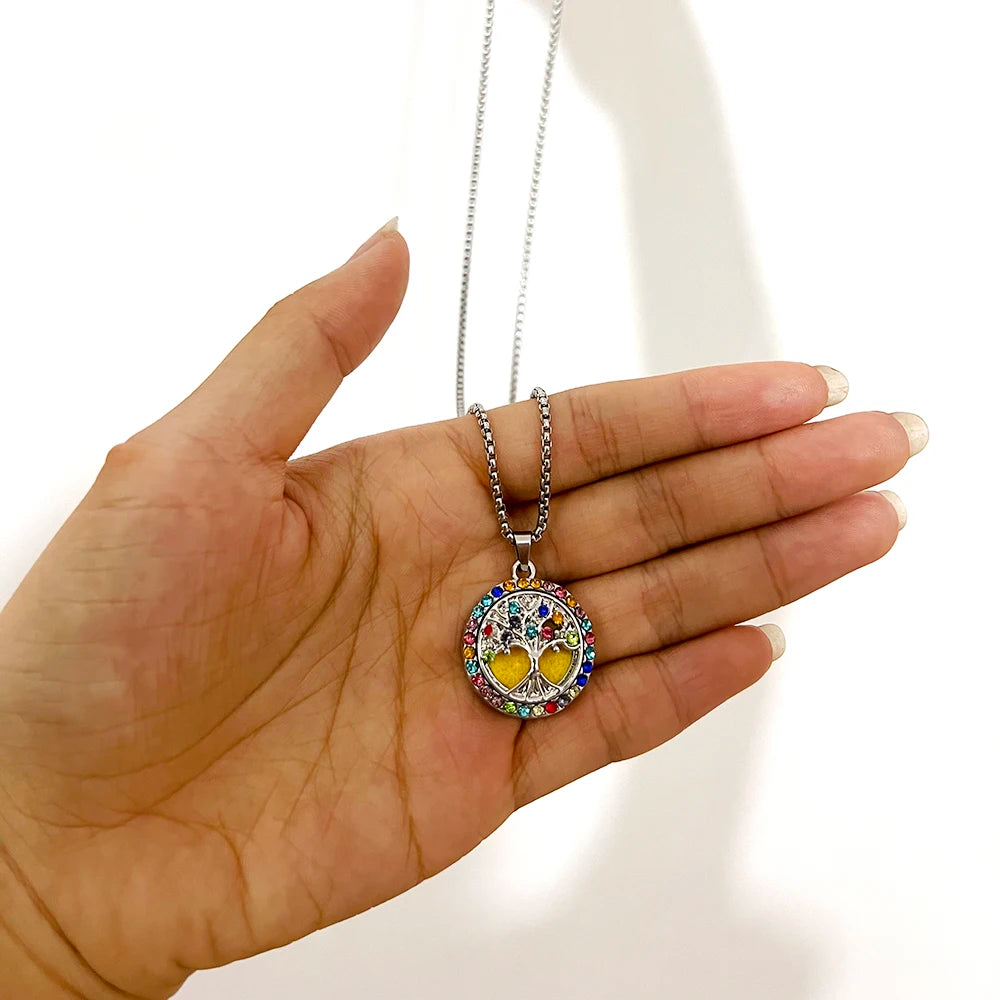 Hand holding a colorful tree of life pendant necklace against a white background