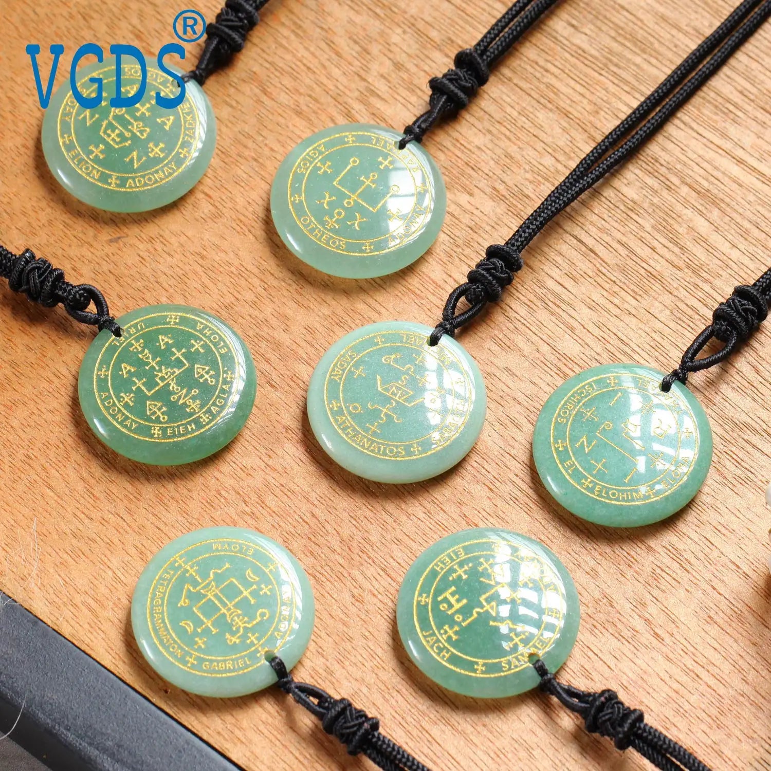 Green stone pendants with symbols on black cords on a wooden surface, branded 'VGDS'.