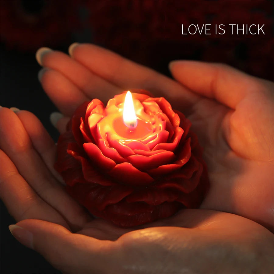 Red rose-shaped candle held in hands with 'LOVE IS THICK' text above
