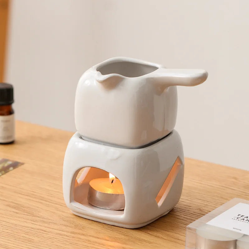 White ceramic oil burner with a lit candle inside on a wooden surface.