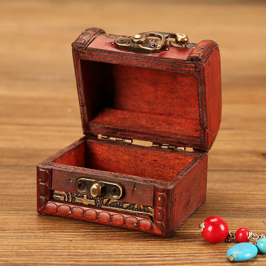 Open red jewelry box with gold accents on a wooden surface, accompanied by colorful earrings.
