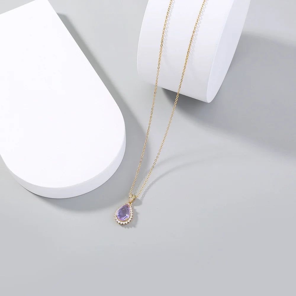 Gold necklace with a purple teardrop pendant on a white surface