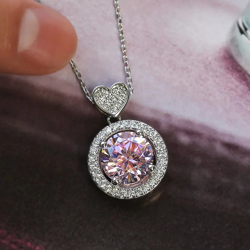 Pink gemstone pendant with heart-shaped top on a chain against a blurred background