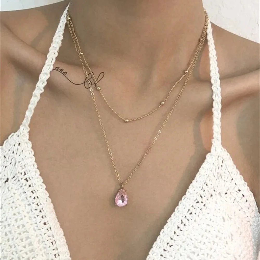 Gold necklace with a pink pendant worn by a person in a white crochet top.
