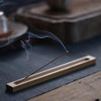 Incense stick burning on a wooden holder with smoke rising, placed on a textured surface.