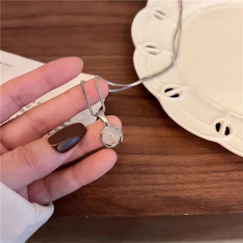 Hand holding a necklace with a pendant on a wooden surface
