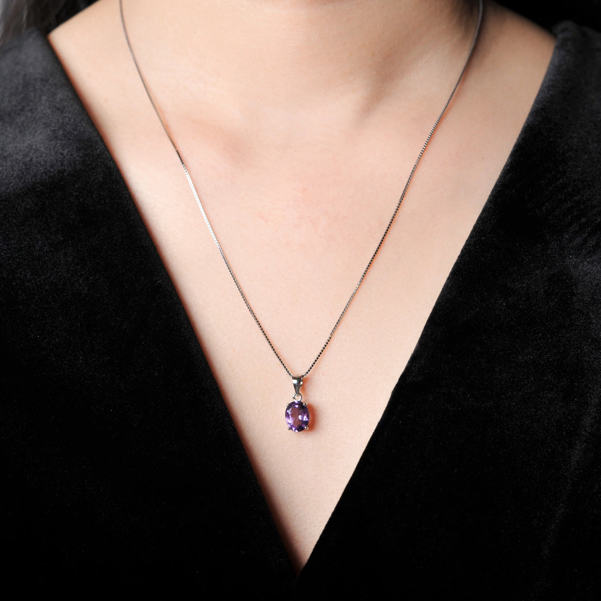 Necklace with a purple pendant worn by a person in a black outfit