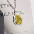 Teardrop-shaped yellow diamond pendant on a chain against a blurred background