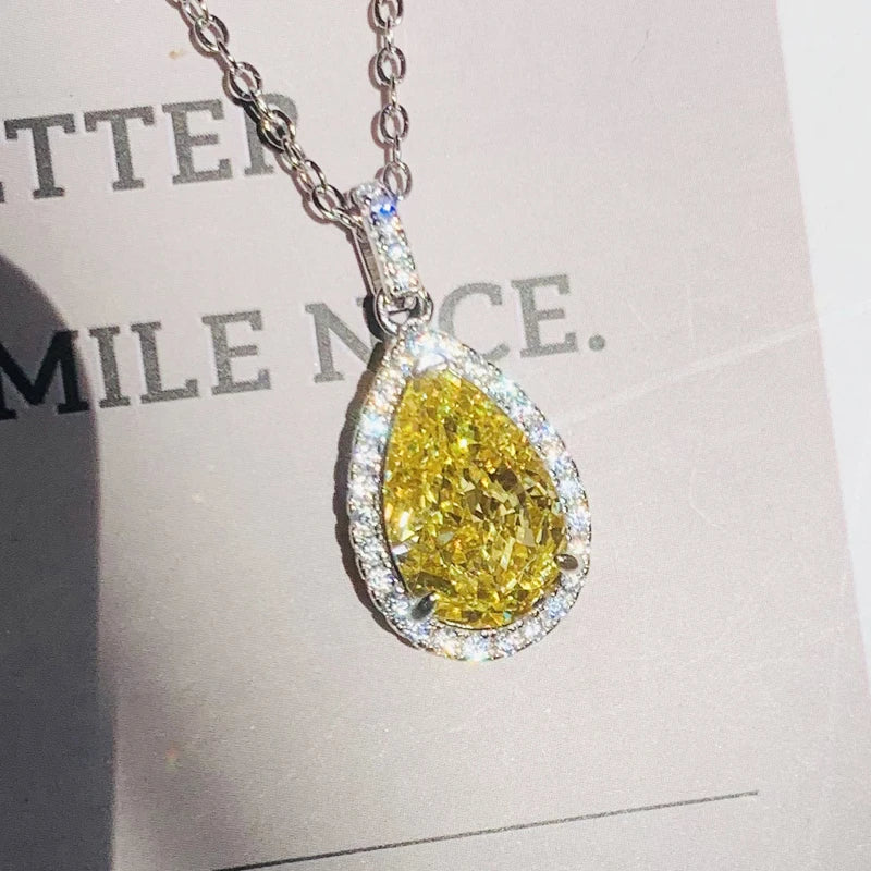 Teardrop-shaped yellow diamond pendant on a chain against a blurred background