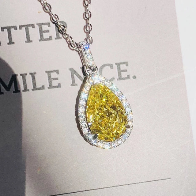Teardrop-shaped yellow diamond pendant on a chain against a blurred background