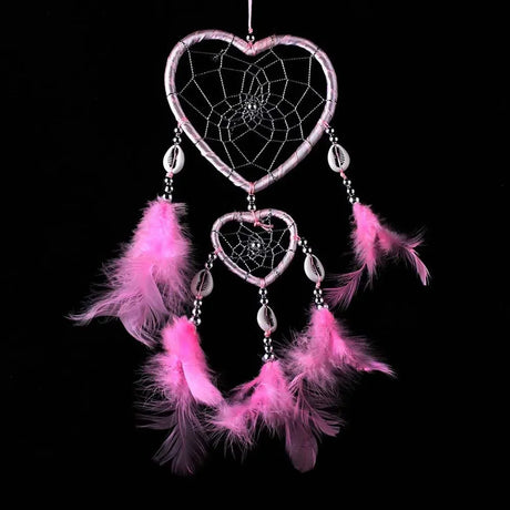 Heart-shaped dreamcatcher with pink feathers on a black background