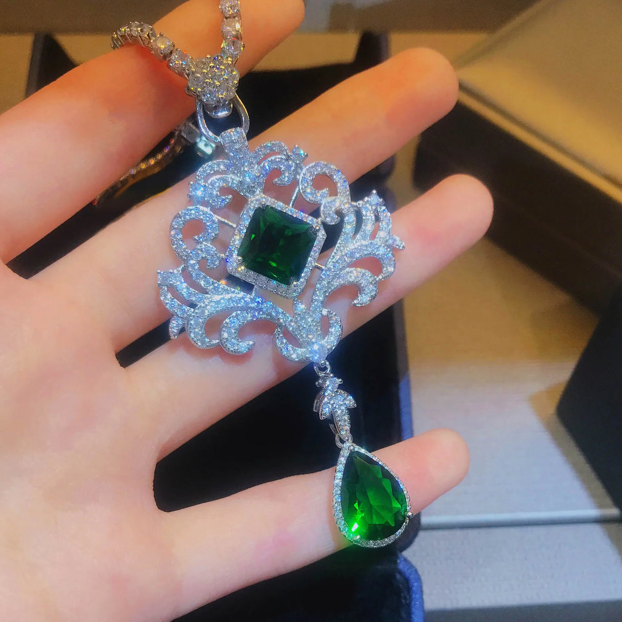 Ornate pendant with green gemstones held in a hand