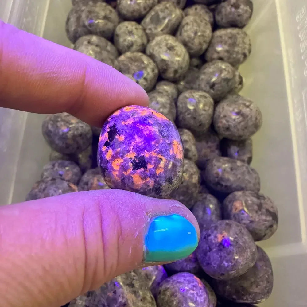 Person holding a glowing purple and orange crystal ball over a container of similar crystals.