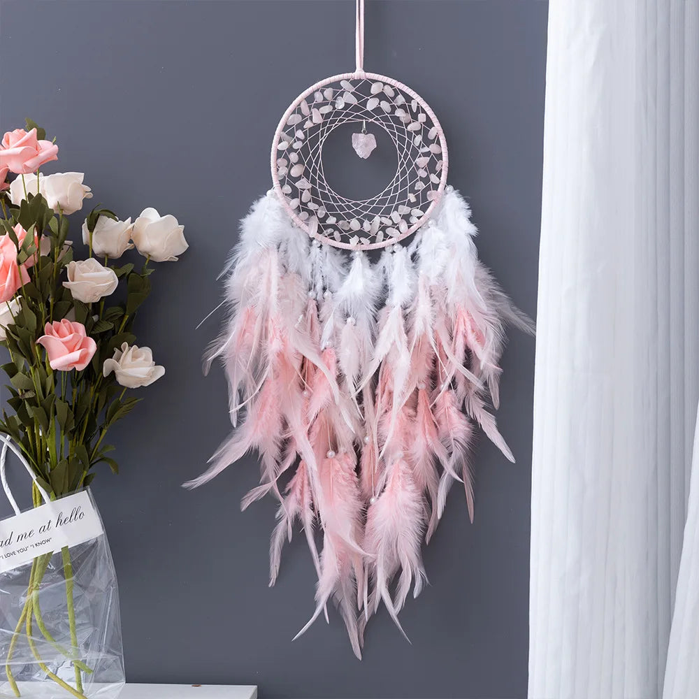 Decorative dreamcatcher with pink and white feathers hanging on a dark gray wall.