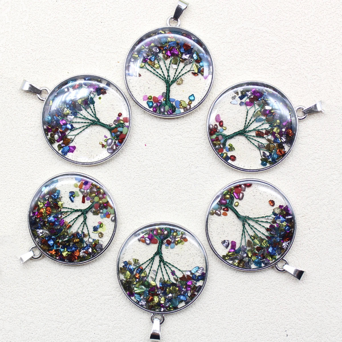 Set of six circular pendants with tree designs and colorful gemstones on a white background