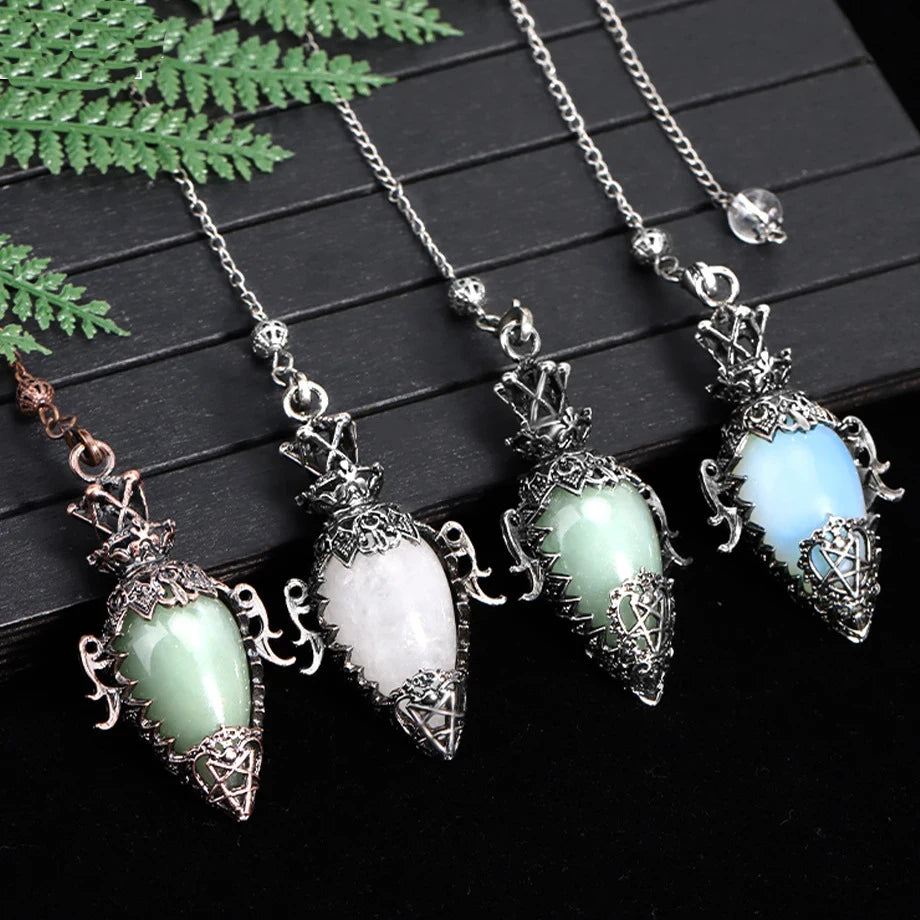 Four pendants with different colored stones on a dark surface with green leaves.