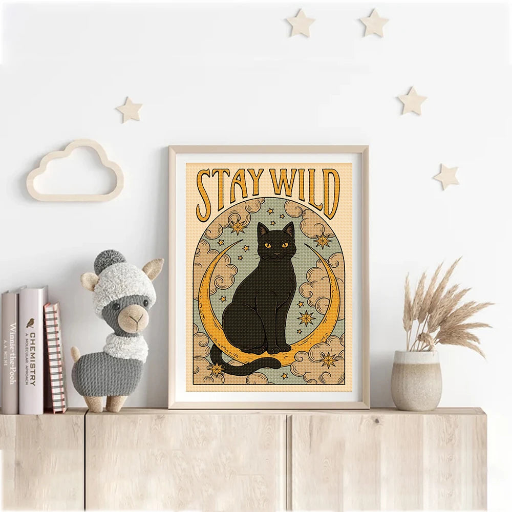 Framed artwork with a black cat illustration and 'Stay Wild' text on a shelf with decorative items.