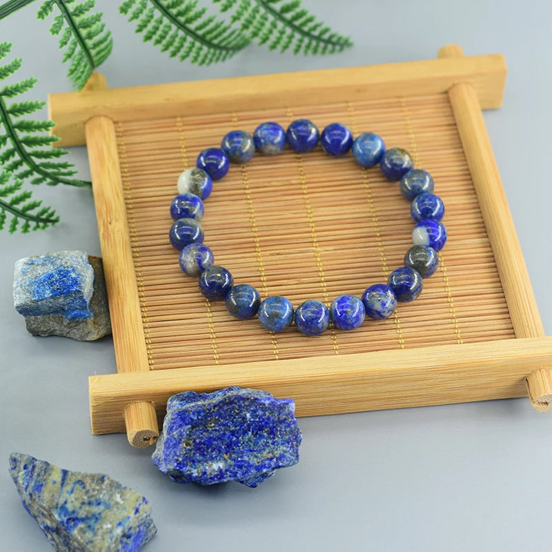 Blue beaded bracelet on a wooden tray with lapis lazuli stones and green leaves in the background