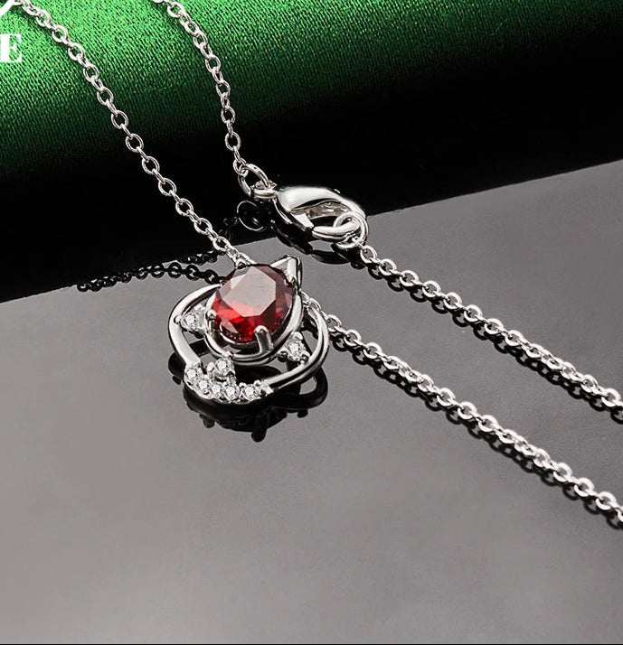 Silver necklace with a red gemstone pendant on a green and gray gradient background