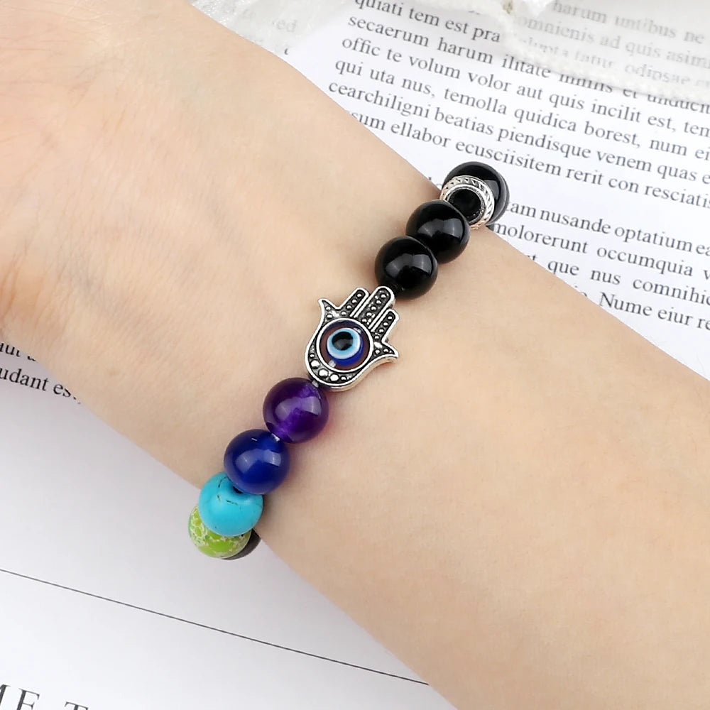 Bracelet with colorful beads and a Hamsa hand charm on a person's wrist, against a blurred text background.