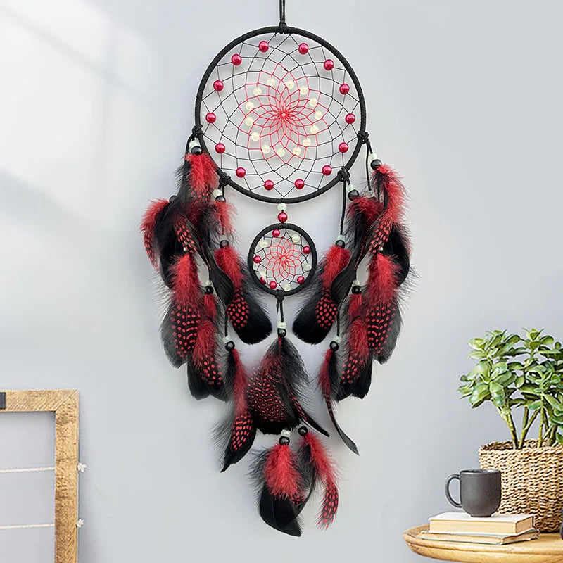 Black and red dreamcatcher on a white wall with a plant and books in the background.