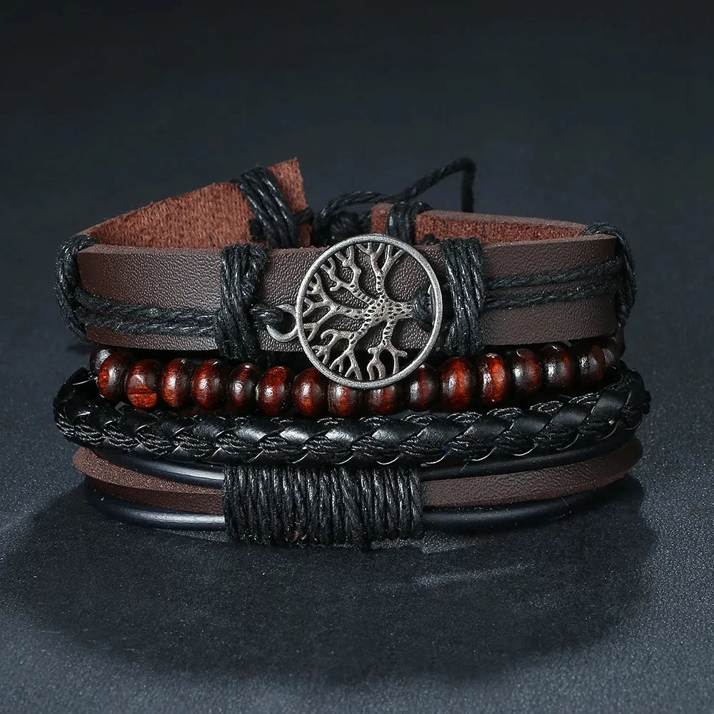 Stack of leather and beaded bracelets with a central metal tree-of-life charm on a dark background