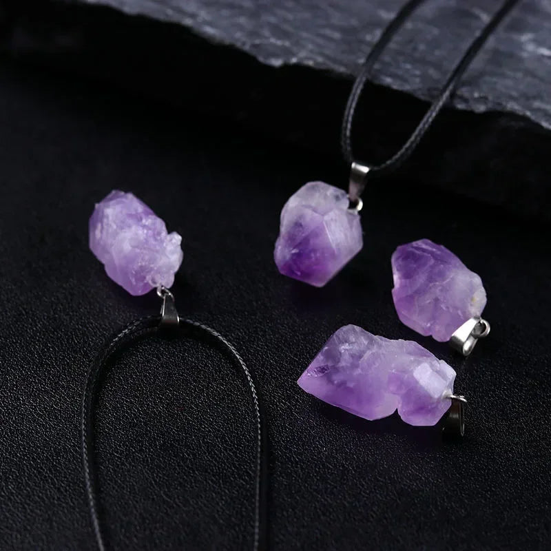 Purple crystal pendants on black leather cords against a dark background