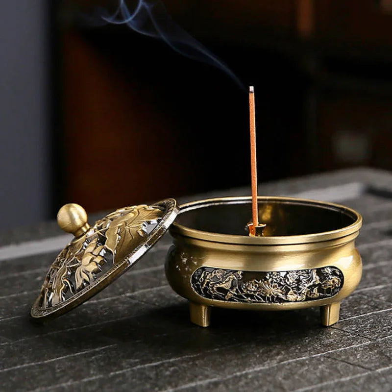 Bronze incense burner with a smoking incense stick on a dark surface