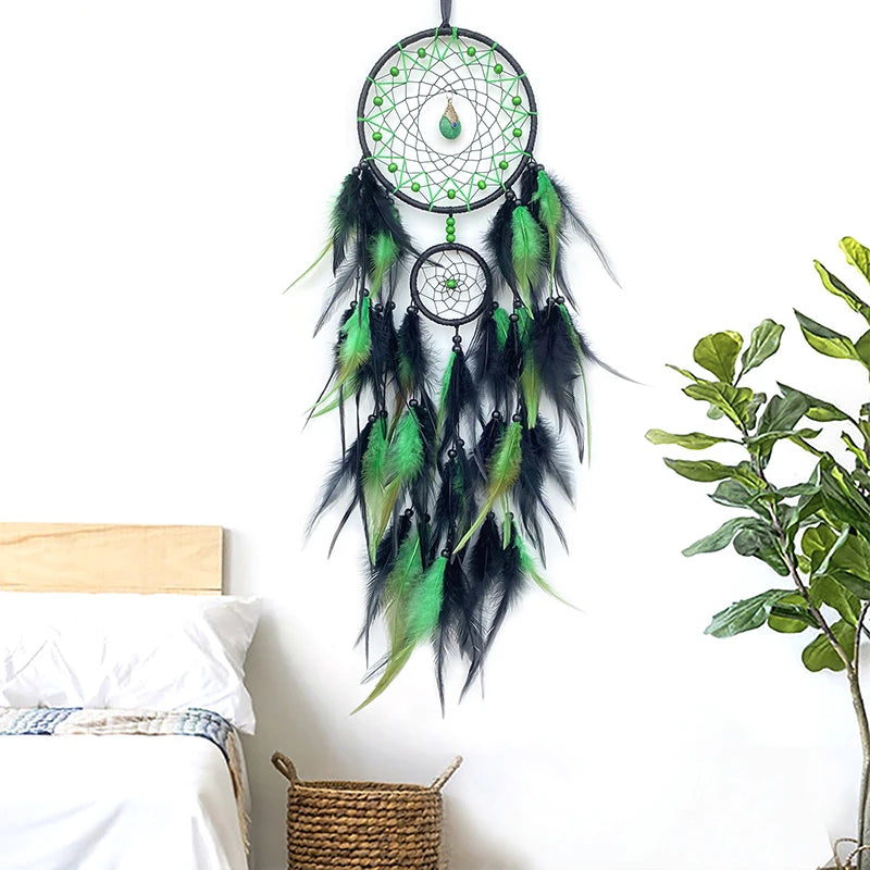 Green and black dreamcatcher hanging on a white wall next to a bed and plant.
